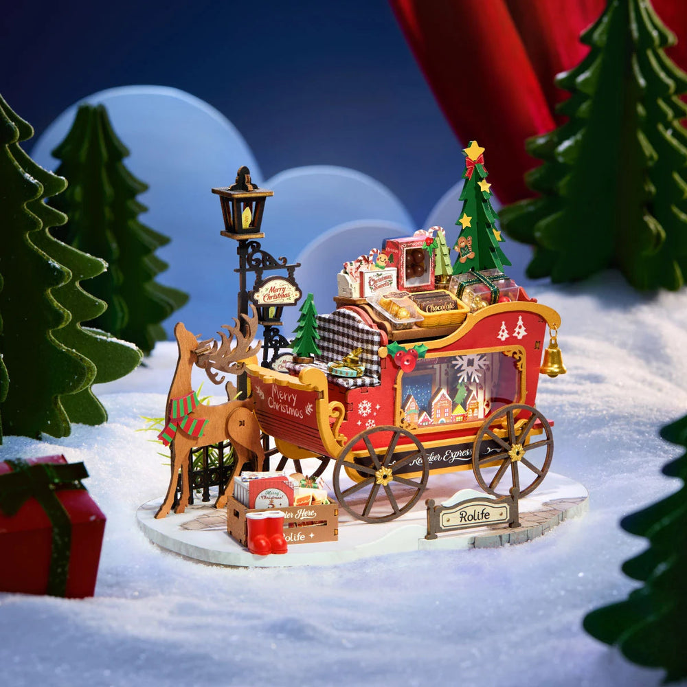 Rolife wooden reindeer and red sleigh miniature on a snowy base with a lamp post, Christmas tree, gifts and candy, set against a blue backdrop with green trees.