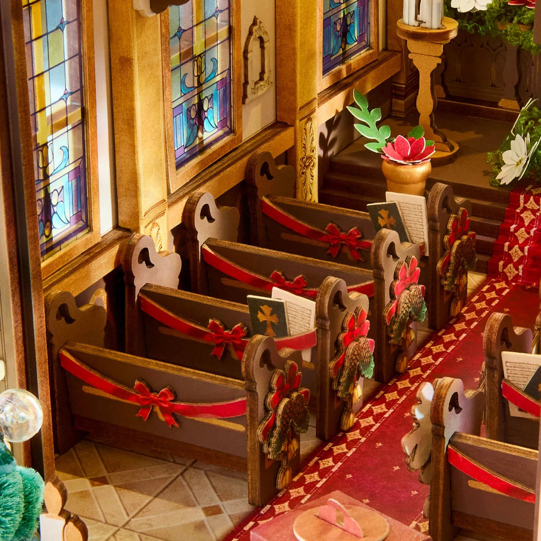 Miniature church pews with red ribbon bows and hymn books beside stained-glass windows and a red carpeted aisle.