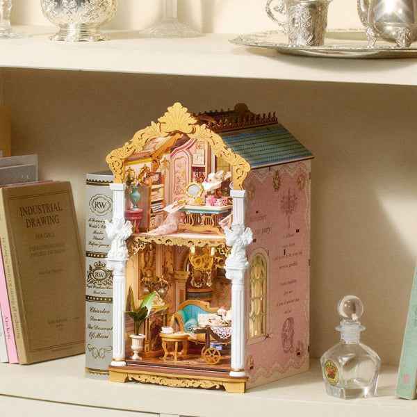 Rolife Rococo Salon TGB24 book nook displayed at an angle on a shelf beside books, showing its pink side panel and two-storey miniature salon