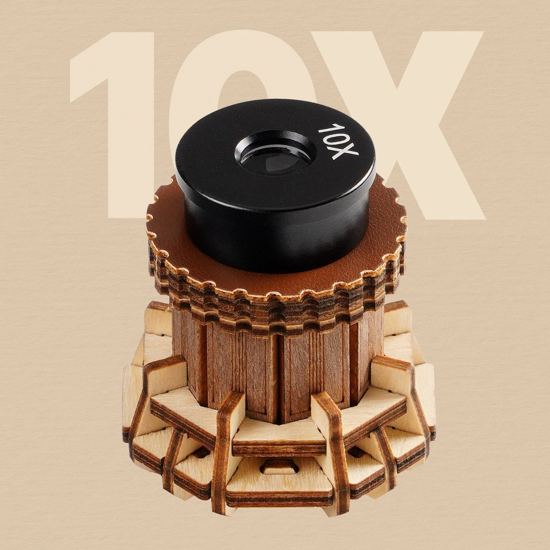 ROKR wooden microscope 10X objective lens shown close-up with a round black lens cap and golden wood gear base on tan background